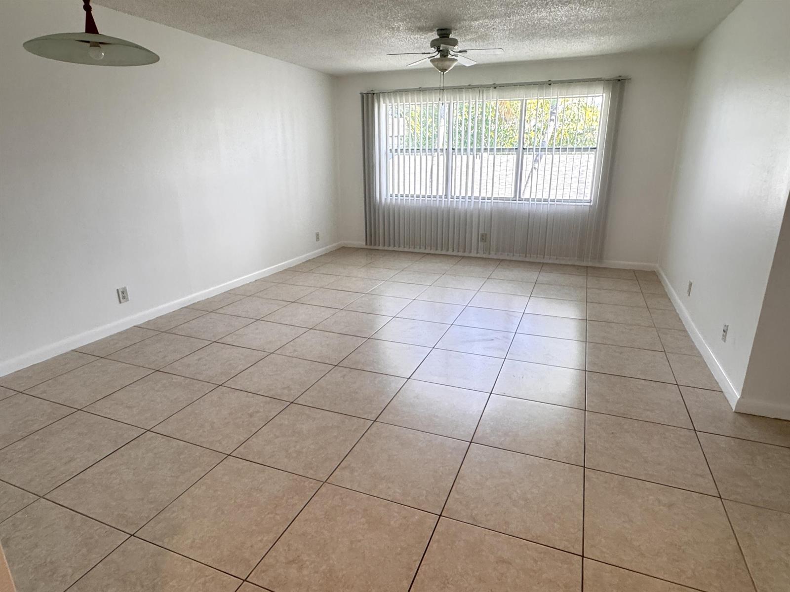 An empty room with beige tile flooring, white walls, a ceiling fan, and vertical blinds — 500 SE 2nd Avenue # 22, Deerfield Beach FL 33441, DEERFIELD BEACH, FL