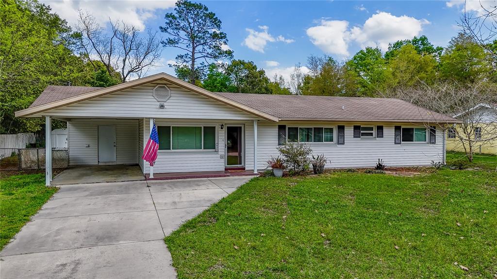 A single-story house with white siding, a carport, and an American flag on the front — 831 NE 41ST AVENUE, OCALA, FL