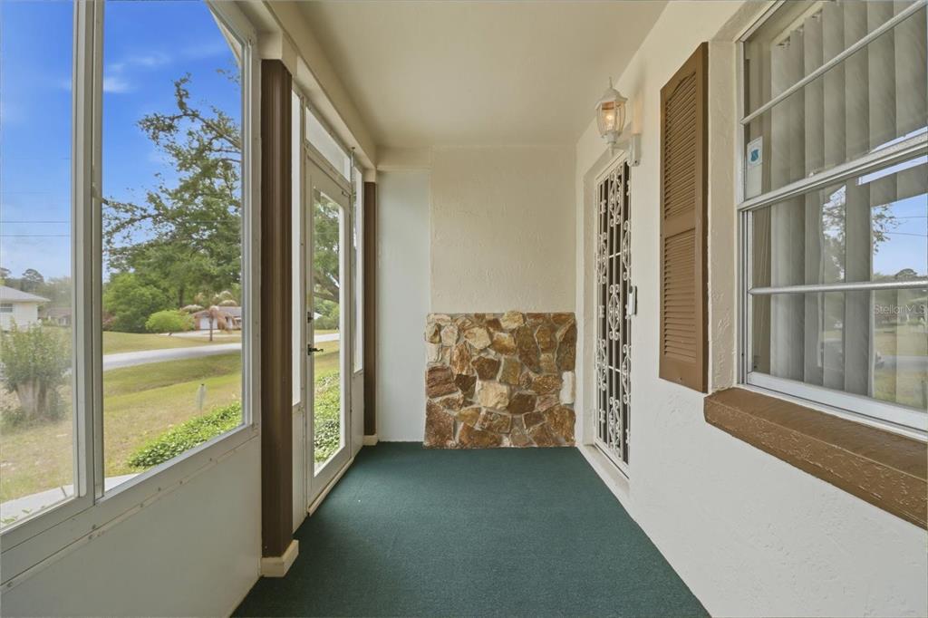 A covered porch features green carpeting, a stone accent wall, and a screened-in entry door — 42 TRUMAN BOULEVARD, BEVERLY HILLS, FL