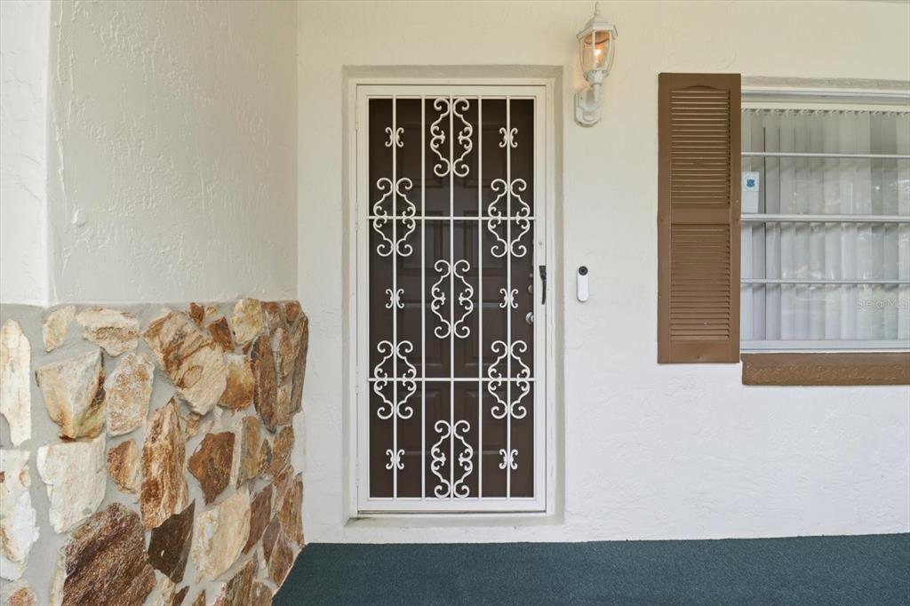 A white front door with a decorative metal security screen sits beside a stone wall — 42 TRUMAN BOULEVARD, BEVERLY HILLS, FL