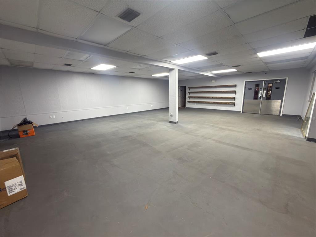 An empty commercial space features gray flooring, white walls, a support pillar, and wall-mounted shelves — 1185 GOODEN CROSSING UNIT A, LARGO, FL