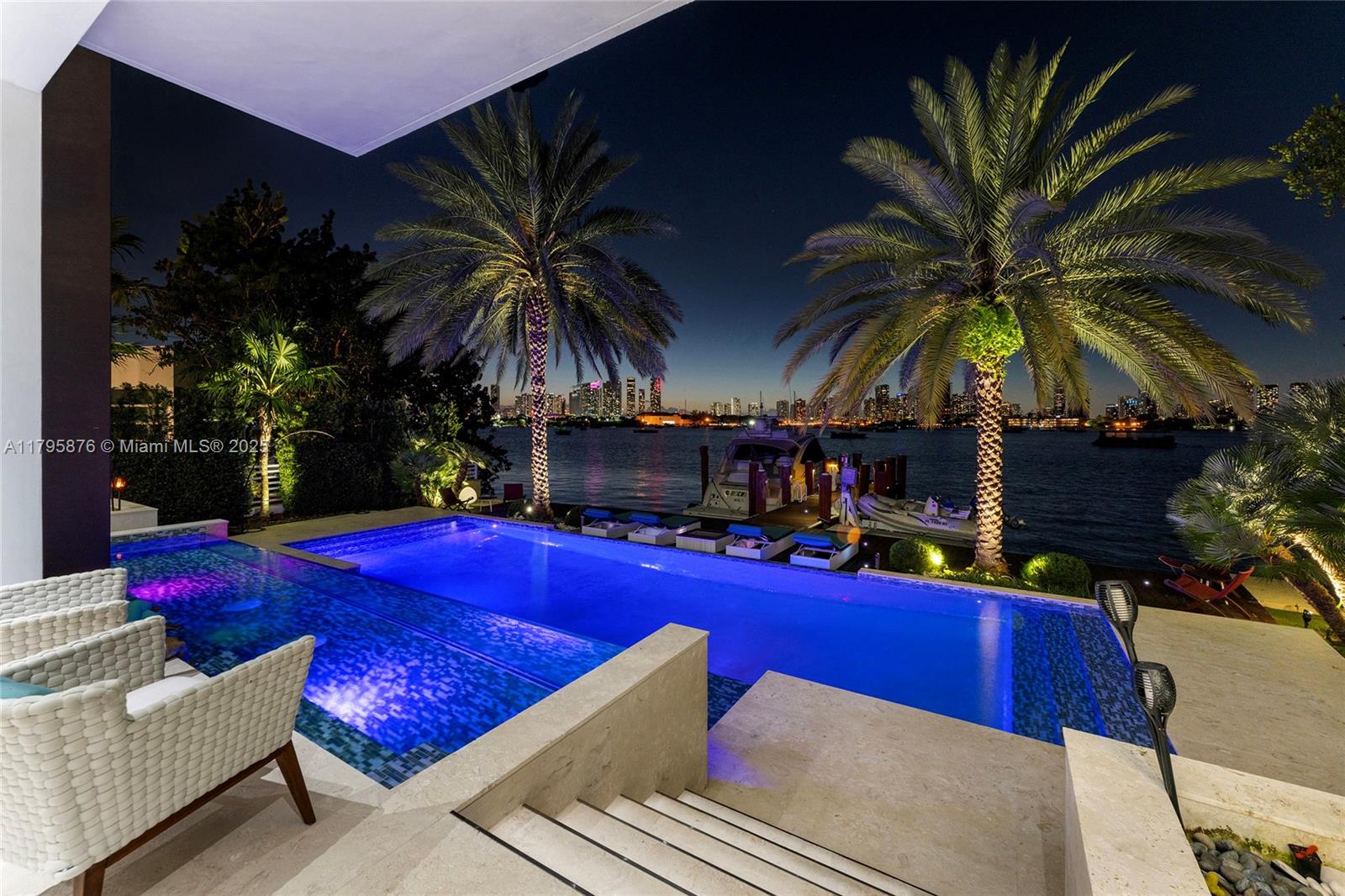 An infinity pool overlooks a bay with a boat dock and city skyline at night — 441 N Hibiscus Dr, Miami Beach FL 33139, MIAMI BEACH, FL
