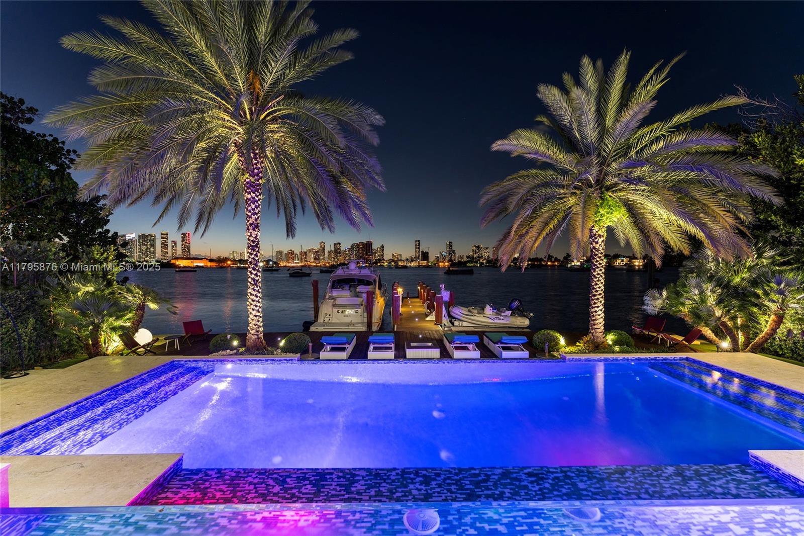 A swimming pool overlooks a dock with boats and a city skyline at night — 441 N Hibiscus Dr, Miami Beach FL 33139, MIAMI BEACH, FL