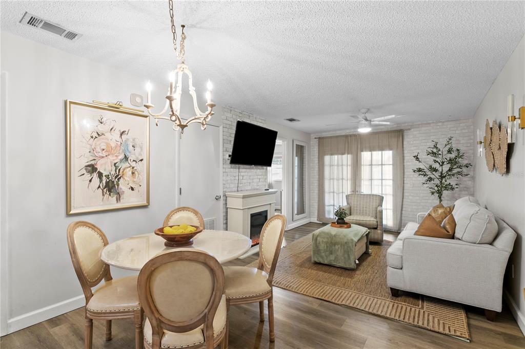 A dining area and living room feature a fireplace, white brick walls, and neutral furniture — 4506 S OAK DRIVE UNIT S92, TAMPA, FL