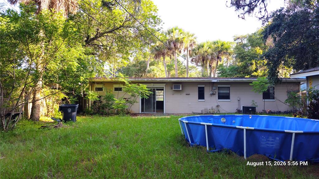 A backyard view of a single-story house featuring a blue above-ground pool and palm trees — 218 OJIBWAY AVENUE, TITUSVILLE, FL