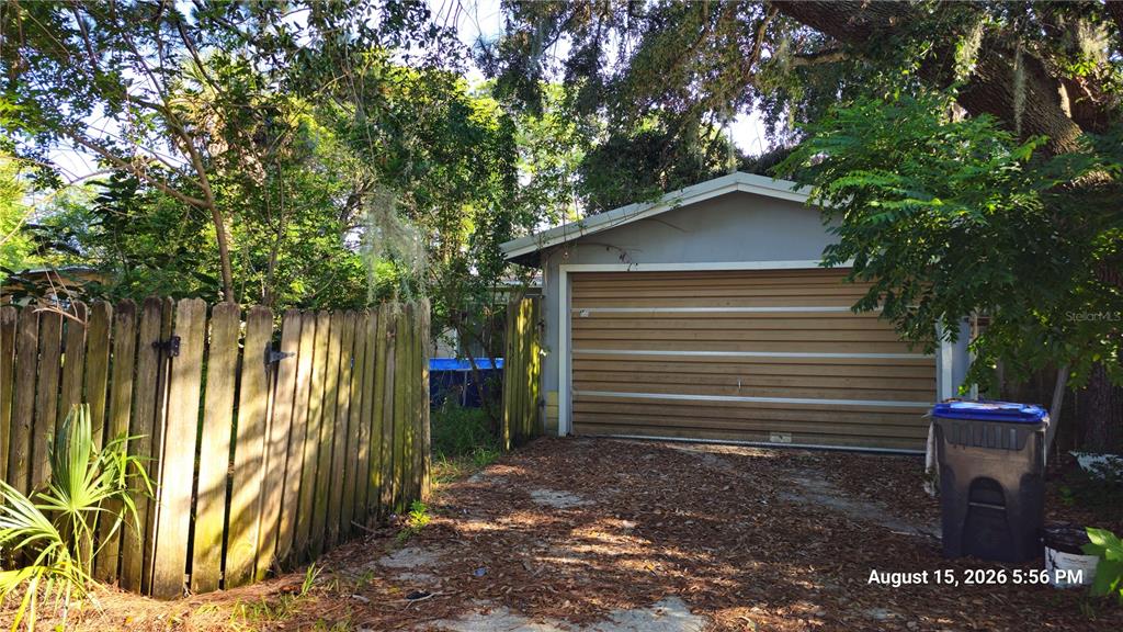 A detached garage with a brown sectional door sits behind a wooden fence and driveway — 218 OJIBWAY AVENUE, TITUSVILLE, FL