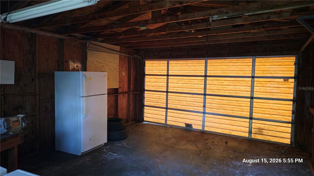 A garage with wood-paneled walls, a concrete floor, a white refrigerator, and a sectional door — 218 OJIBWAY AVENUE, TITUSVILLE, FL