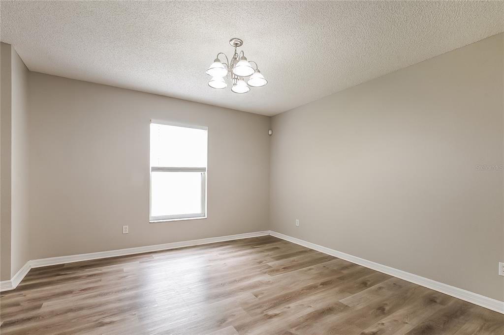 An empty room features light-colored walls, wood-look flooring, and a central multi-light chandelier — 14332 ABINGTON HEIGHTS DRIVE, ORLANDO, FL