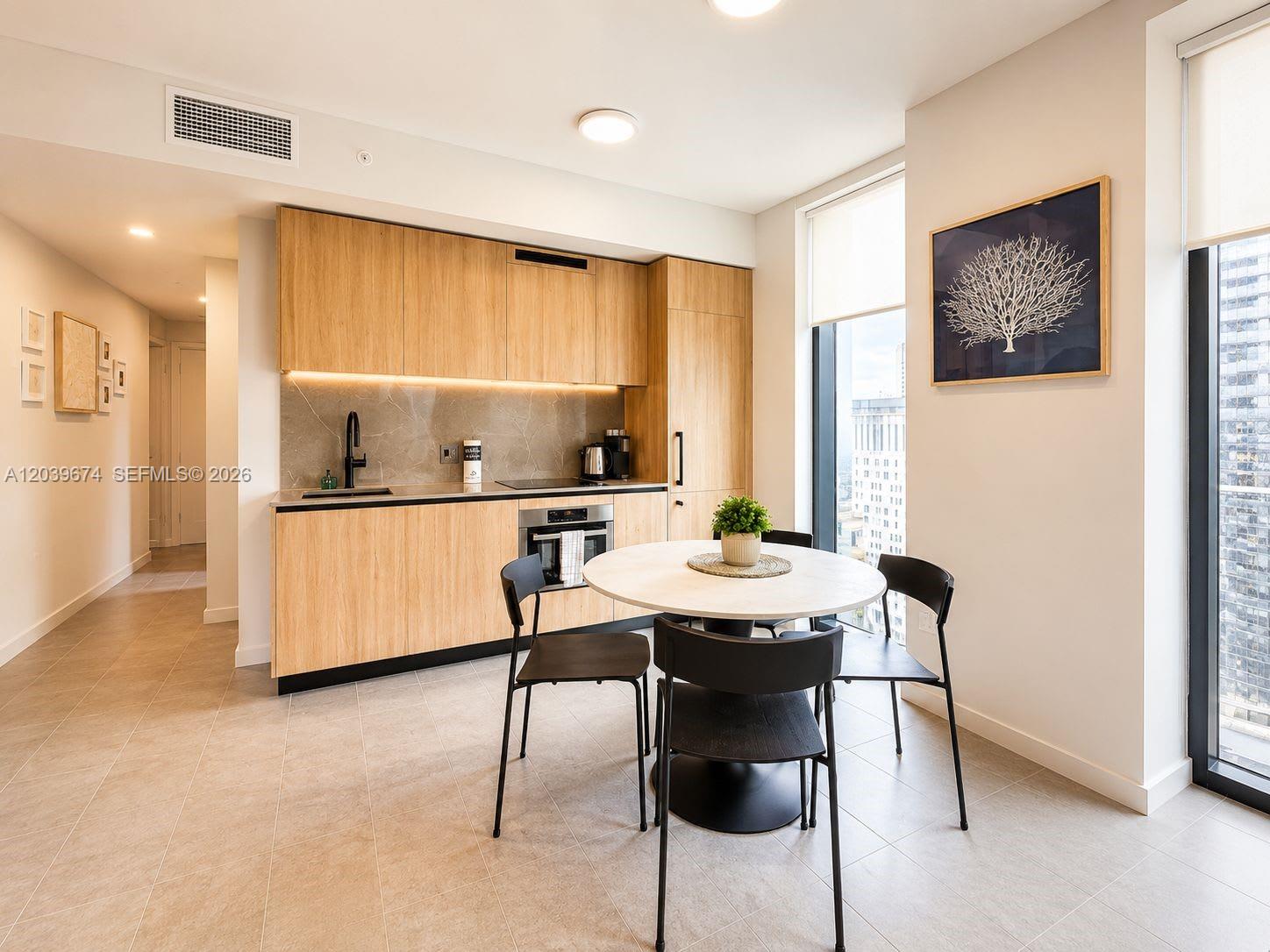 A modern kitchen features light wood cabinetry, a round dining table, and floor-to-ceiling windows — 121 NE 5th St # 2408, Miami FL 33132, MIAMI, FL