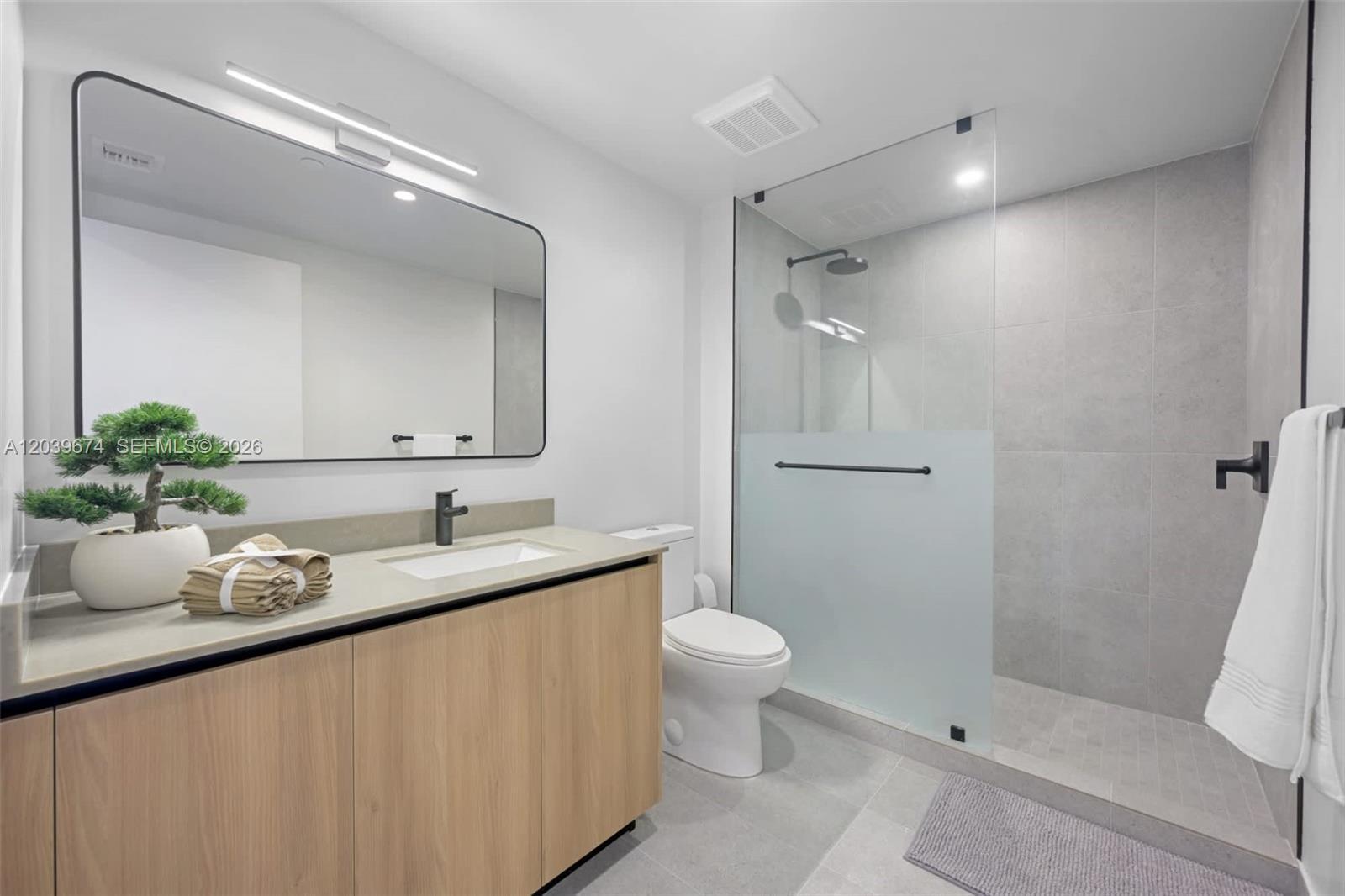 A modern bathroom features a light wood vanity, a walk-in shower, and a large mirror — 121 NE 5th St # 2408, Miami FL 33132, MIAMI, FL