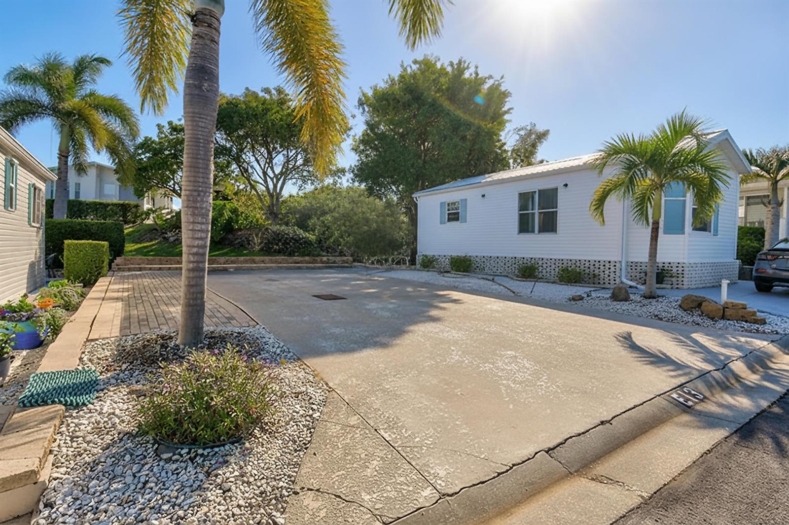 A white manufactured home sits behind a concrete driveway with palm trees and landscaping — 900 Juno Ocean Walk, Juno Beach FL 33408, JUNO BEACH, FL