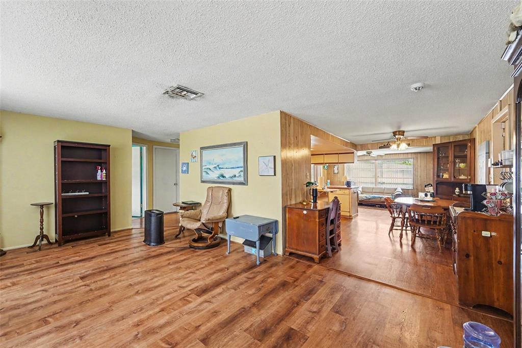 A living room with wood-look flooring, yellow walls, and an open transition to the dining area — 7015 MORAVIAN DRIVE, PORT RICHEY, FL
