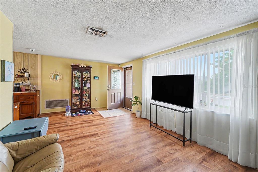 A living room with yellow walls, wood-look flooring, a television on a stand, and a door — 7015 MORAVIAN DRIVE, PORT RICHEY, FL
