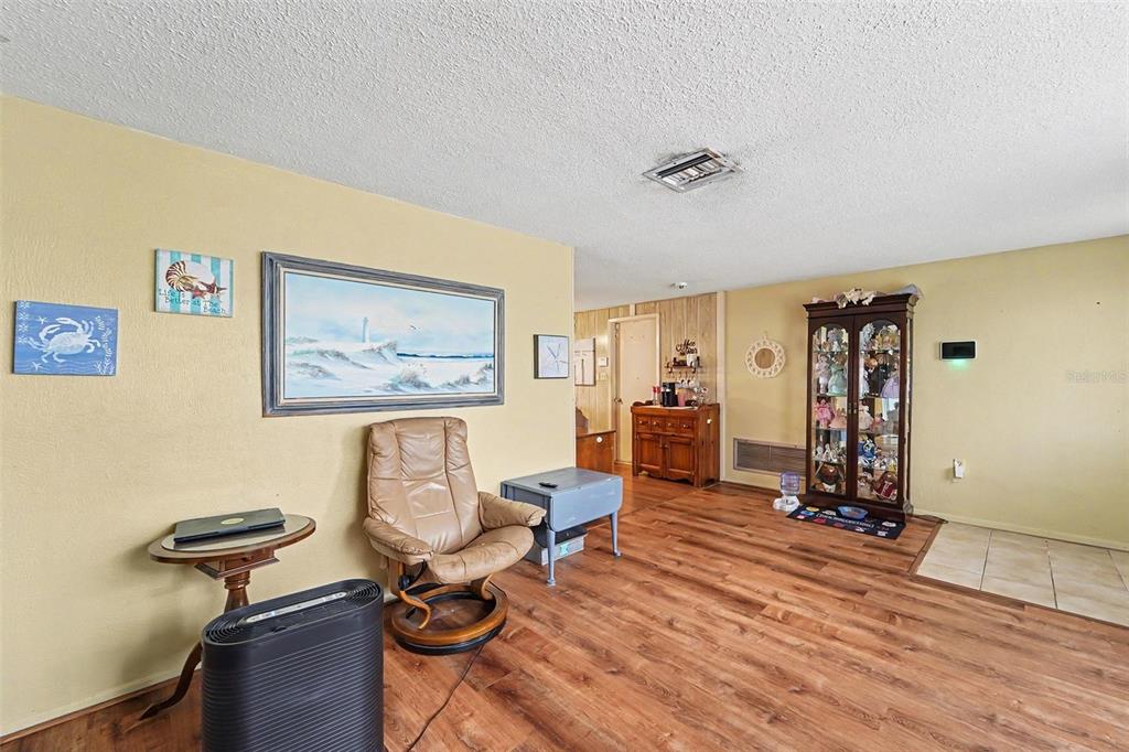 A living room with wood-look flooring, a tan wall, a recliner, and a display cabinet — 7015 MORAVIAN DRIVE, PORT RICHEY, FL