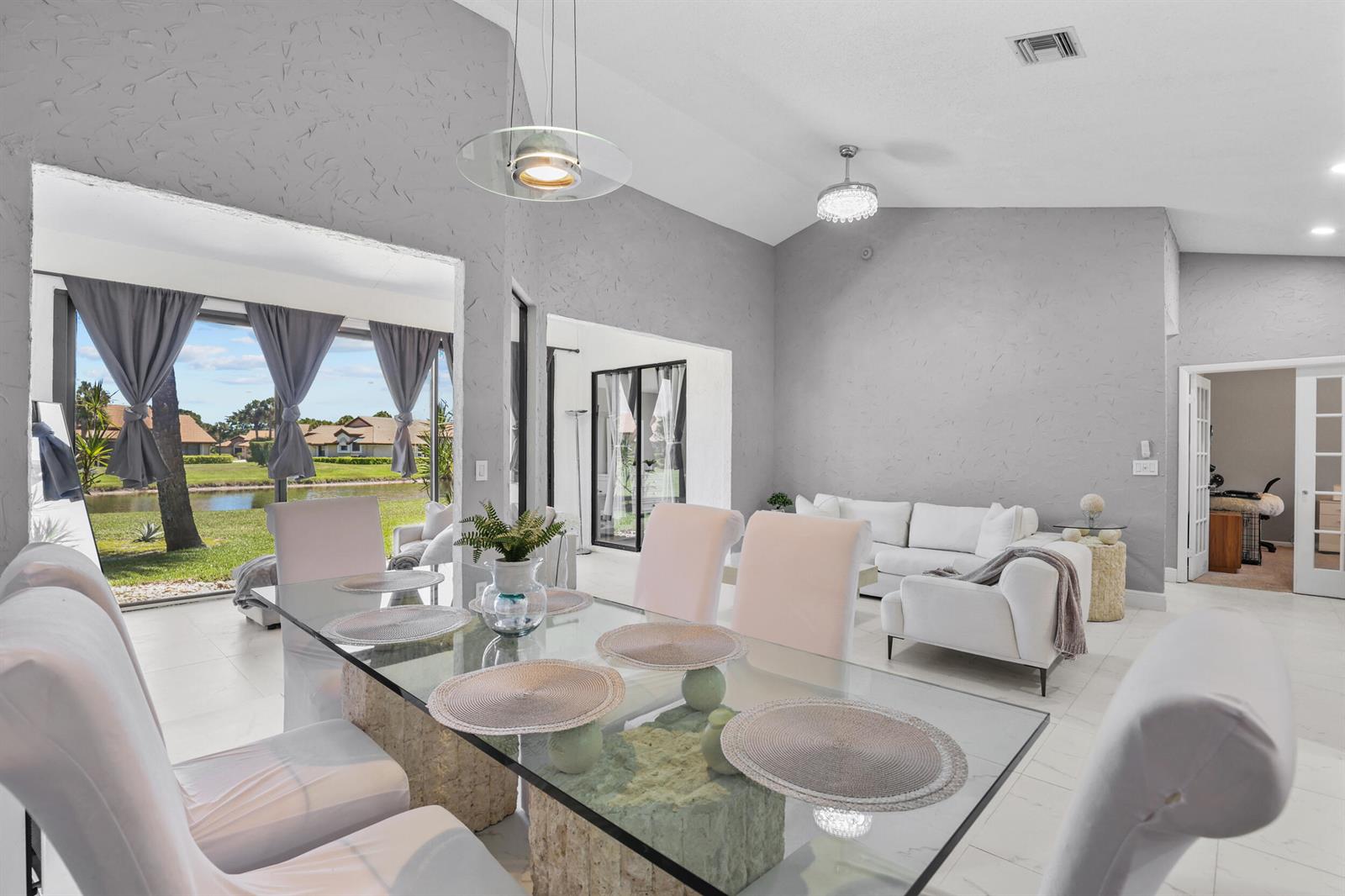 A dining area with a glass table overlooks a lake through large sliding glass doors — 8180 Bellwort Place, Boynton Beach FL 33472, BOYNTON BEACH, FL