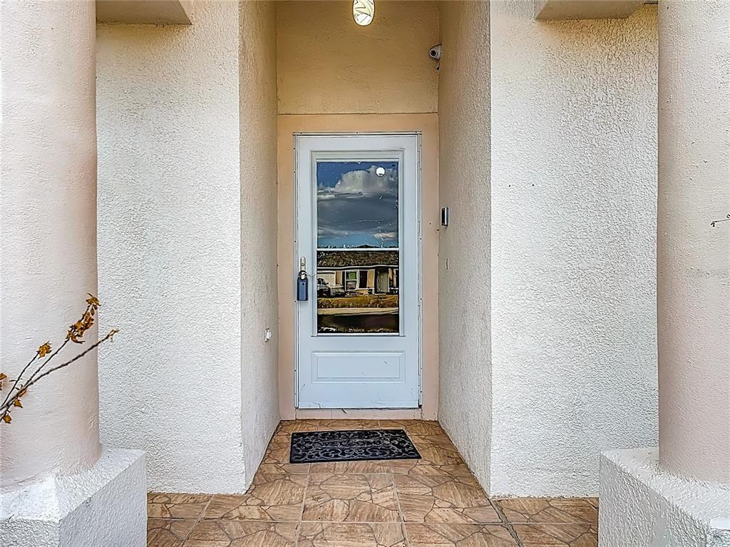 A white front door with a glass insert sits between two pillars on a tiled porch — 1910 DOLPHIN DRIVE, KISSIMMEE, FL