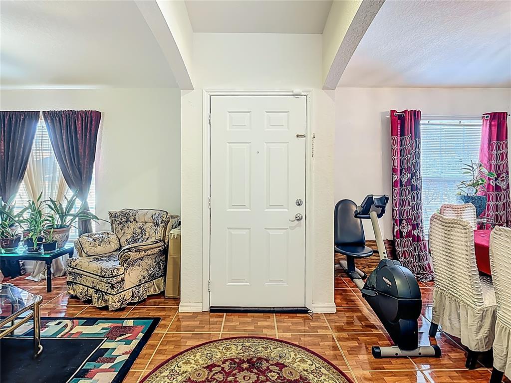 A room with a white front door, tile flooring, an armchair, and an exercise bike — 1910 DOLPHIN DRIVE, KISSIMMEE, FL