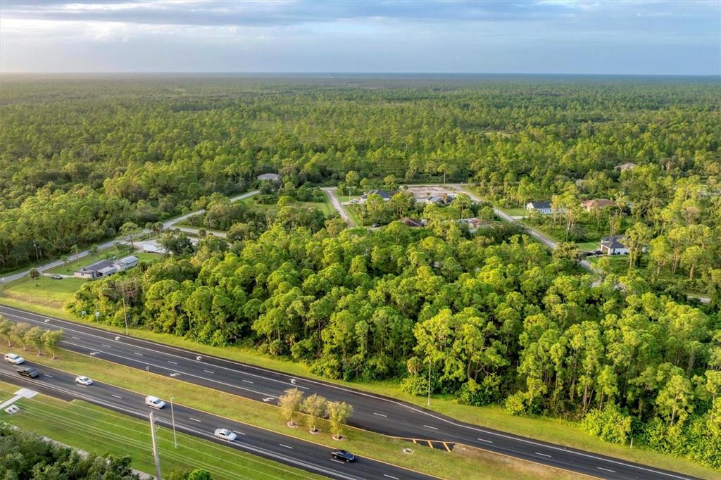 An aerial view shows a wooded lot adjacent to a multi-lane highway and residential houses — 11201 TAMIAMI TRAIL S, NORTH PORT, FL