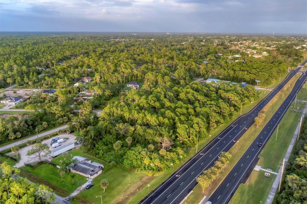 An aerial view shows a wooded lot adjacent to a multi-lane highway and residential houses — 11201 TAMIAMI TRAIL S, NORTH PORT, FL