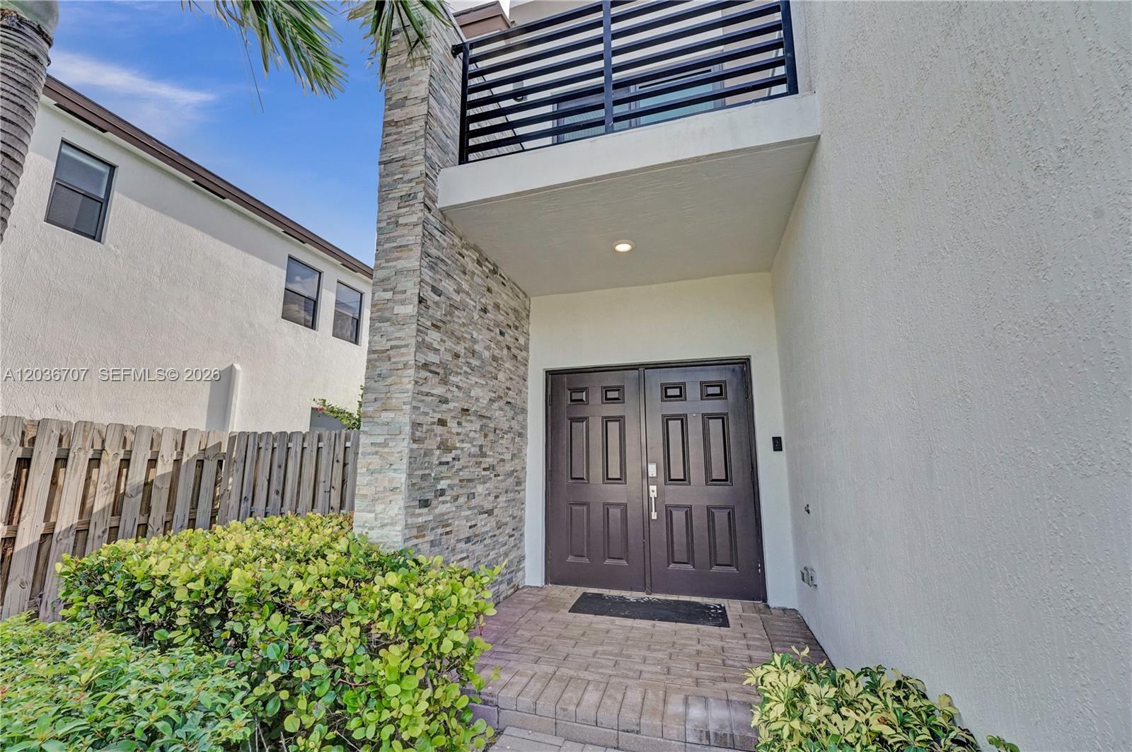 The exterior view shows a double front door, stone veneer siding, and a second-story balcony — 20900 NE 2nd Ct, Miami FL 33179, MIAMI, FL