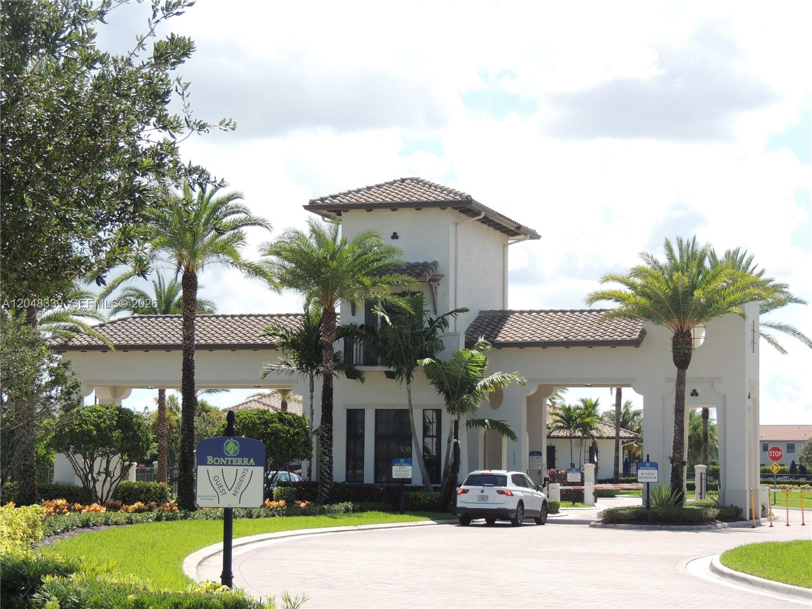 The gated entrance to a residential community features a white guardhouse and palm trees — 9336 W 34th Ct, Hialeah FL 33018, HIALEAH, FL