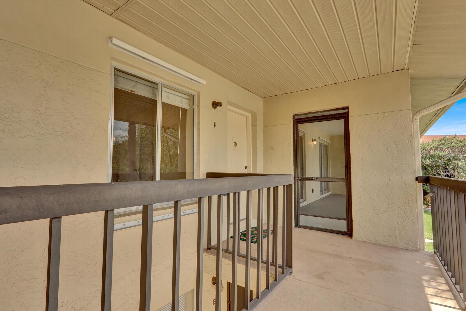 An exterior view of a second-story apartment balcony featuring a brown railing and door F — 6563 Chasewood Drive # F, Jupiter FL 33458, JUPITER, FL