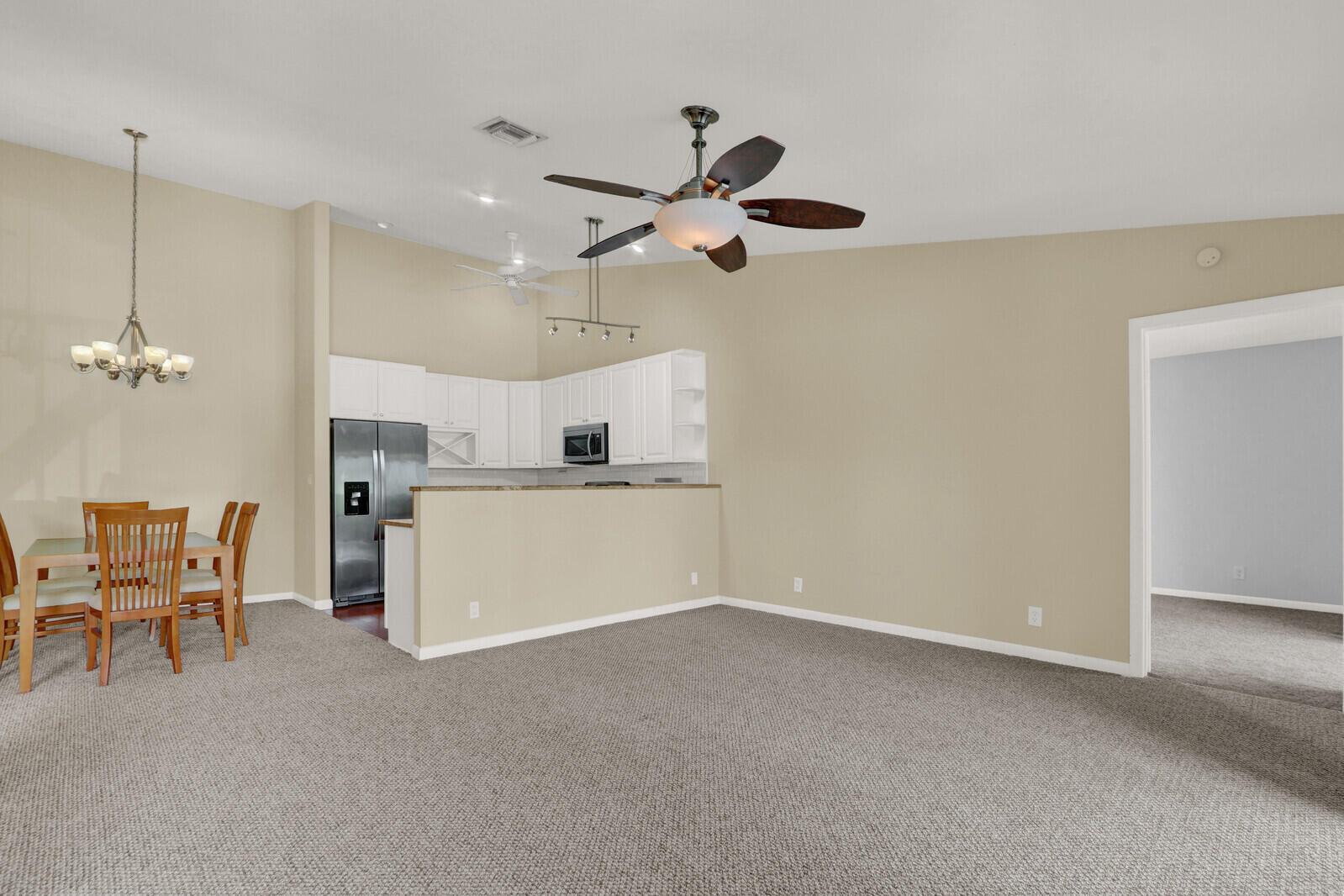 A living room with beige walls, gray carpeting, a ceiling fan, and an open kitchen — 6563 Chasewood Drive # F, Jupiter FL 33458, JUPITER, FL