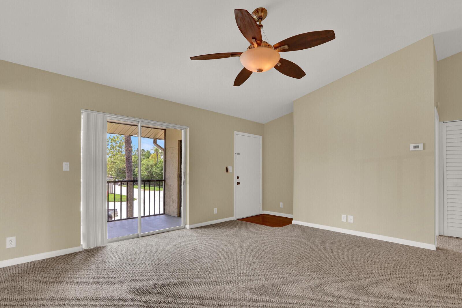 An empty living room features beige walls, tan carpeting, a ceiling fan, and a sliding door — 6563 Chasewood Drive # F, Jupiter FL 33458, JUPITER, FL