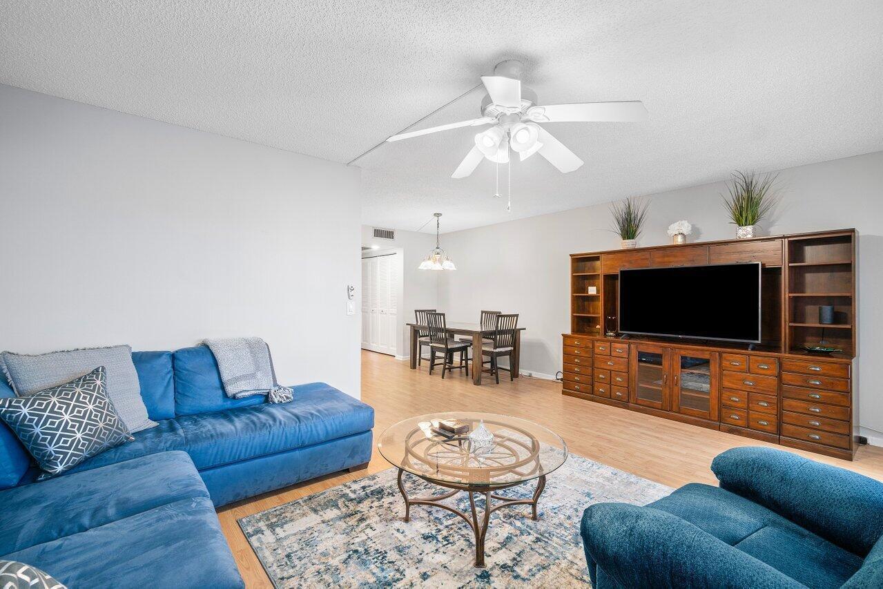 A living room features a blue sectional sofa, a glass coffee table, and wood cabinetry — 2046 Rexford C, Boca Raton FL 33434, BOCA RATON, FL