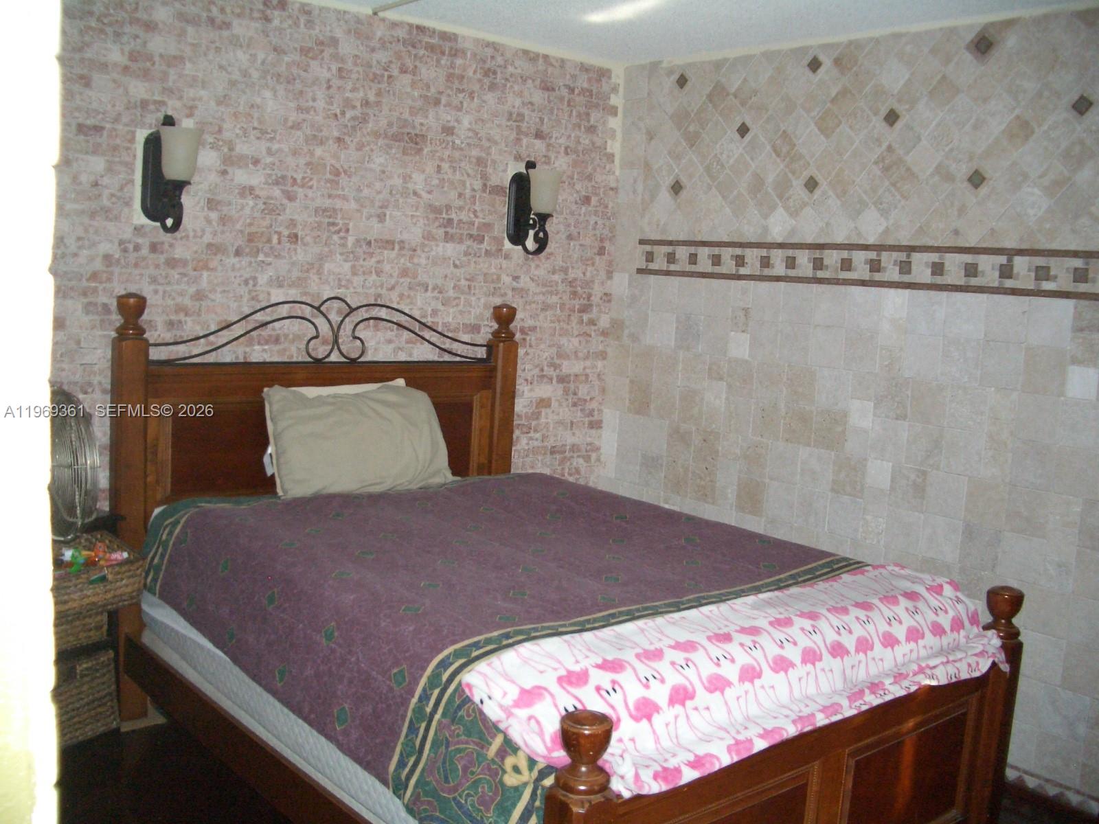 A bedroom features a wooden bed, brick-patterned wallpaper, and a tiled accent wall — 10900 SW 104th St # 324, Miami FL 33176, MIAMI, FL