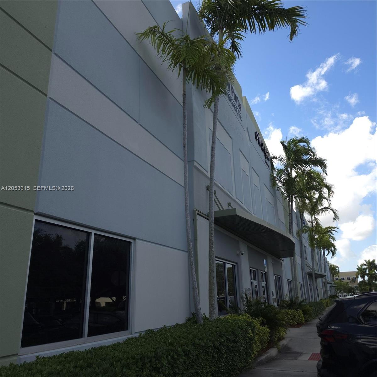 A low-angle exterior view shows a multi-story commercial building with palm trees and landscaping — SWEETWATER, FL