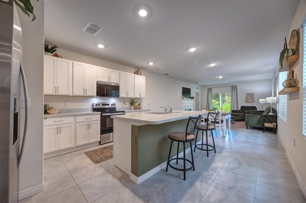 A kitchen with white cabinets, a green island, and stainless steel appliances opens to a living area — 372 PELHAM PARK DRIVE, DELAND, FL