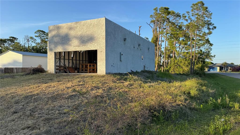 An unfinished concrete building sits on a grassy lot with trees in the background — 5182 HOPKINS AVENUE, PORT CHARLOTTE, FL