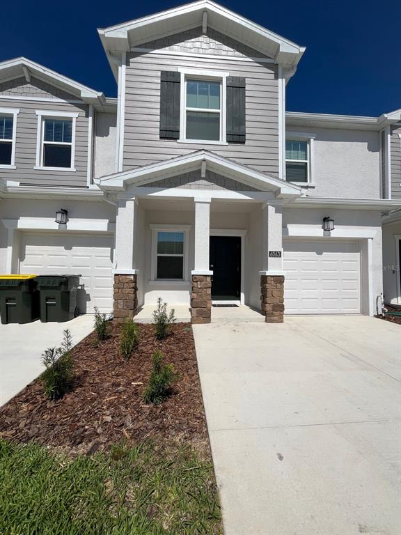 The exterior of a two-story townhouse features a stone-accented entryway, a garage, and landscaping — 6063 PEACEFUL PARK WAY, CLERMONT, FL
