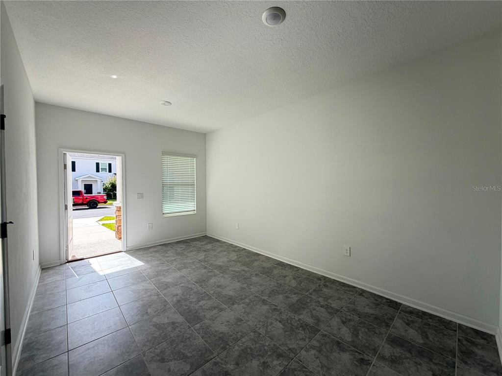 An empty room features gray tile flooring, white walls, a window, and an open exterior door — 6063 PEACEFUL PARK WAY, CLERMONT, FL
