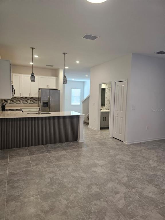 A kitchen with white cabinets, a gray island, and tile flooring opens to a hallway — 6063 PEACEFUL PARK WAY, CLERMONT, FL
