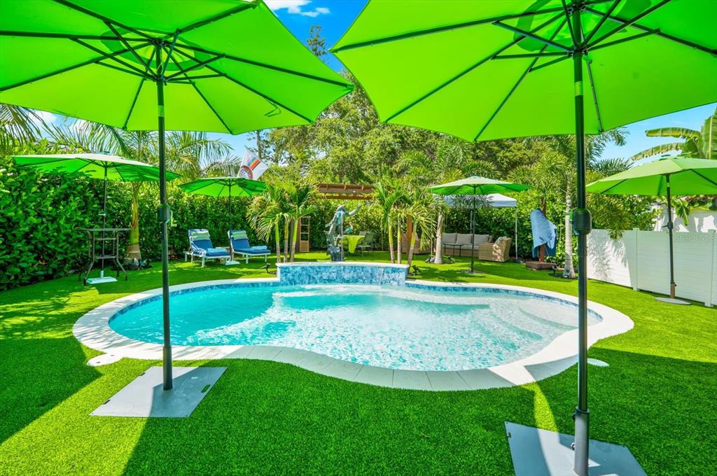 A backyard swimming pool is surrounded by artificial turf, lounge chairs, and several green umbrellas — 127 23RD STREET N, ST PETERSBURG, FL