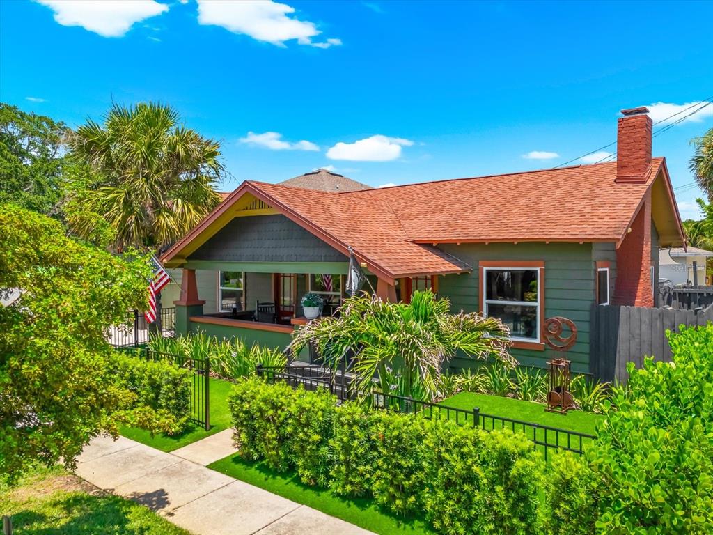 A green bungalow with a red roof and a front porch sits behind a hedge — 127 23RD STREET N, ST PETERSBURG, FL