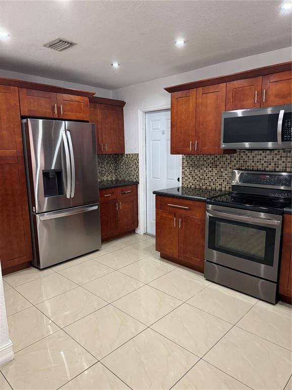 A kitchen features cherry wood cabinets, stainless steel appliances, and light-colored tile flooring — 8240 NW 181ST STREET, HIALEAH, FL