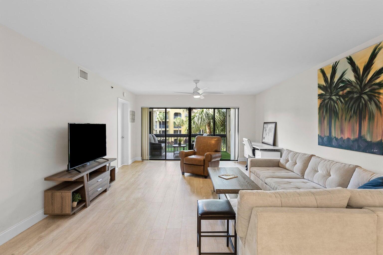 A living room with light wood floors, a beige sectional sofa, and a balcony view — 700 Uno Lago Drive # 303, Juno Beach FL 33408, JUNO BEACH, FL