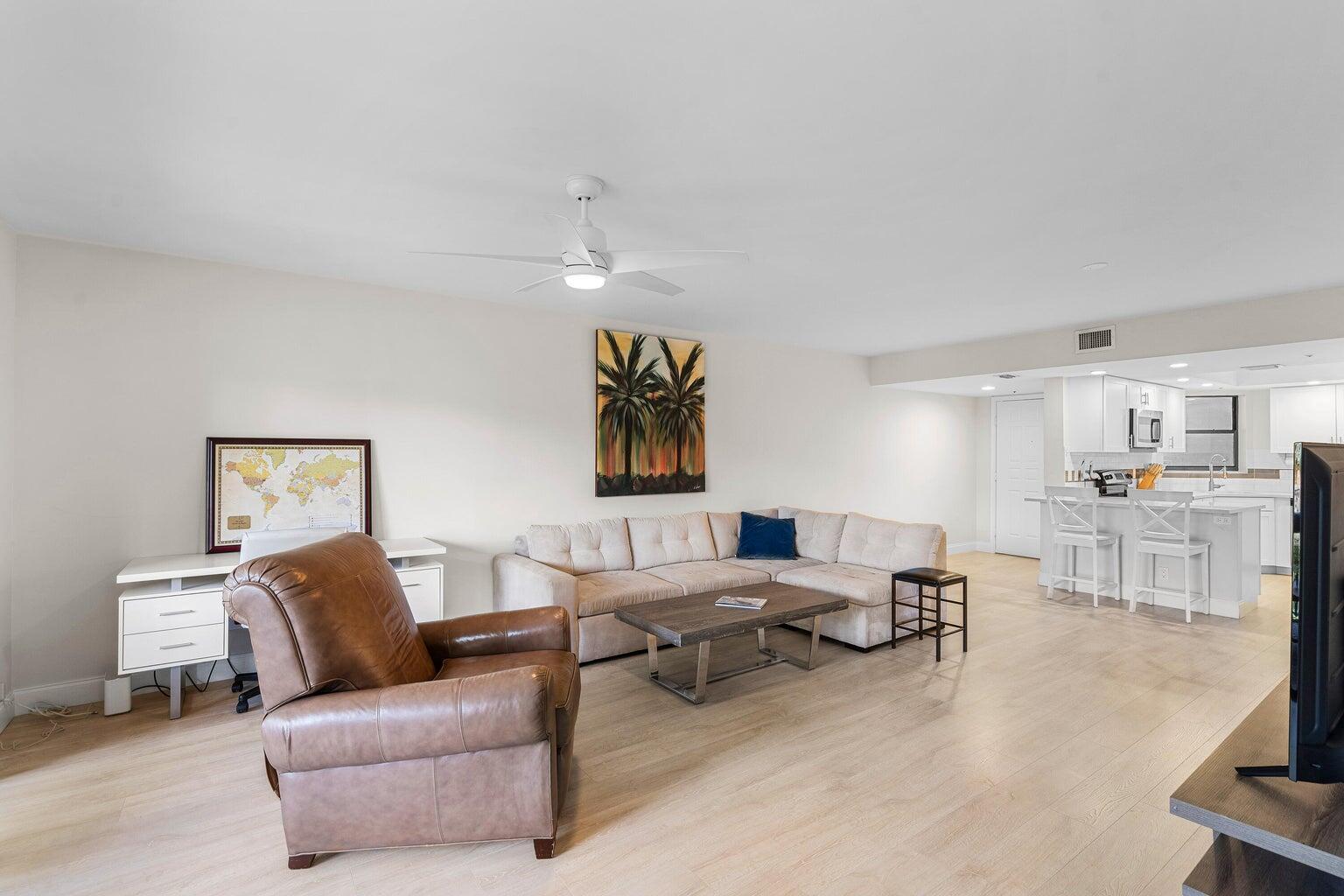 A living room with light wood floors, a beige sectional, and an open kitchen — 700 Uno Lago Drive # 303, Juno Beach FL 33408, JUNO BEACH, FL