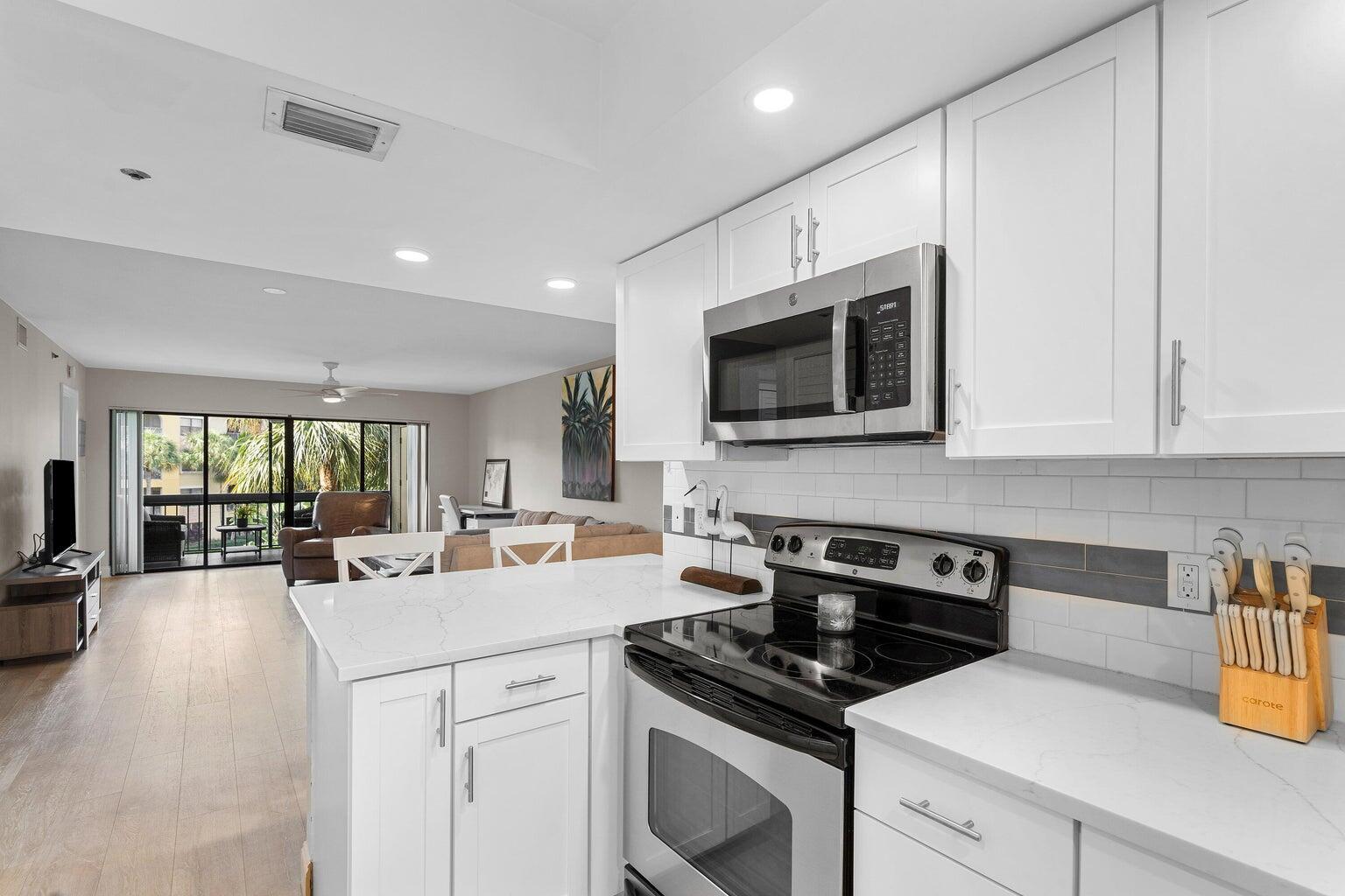 A white kitchen with quartz countertops and stainless steel appliances overlooks an open living area — 700 Uno Lago Drive # 303, Juno Beach FL 33408, JUNO BEACH, FL
