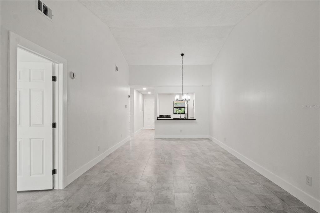 A bright, empty room features light gray tile flooring, white walls, and a kitchen pass-through — 7828 NIAGARA AVENUE UNIT 322, TAMPA, FL