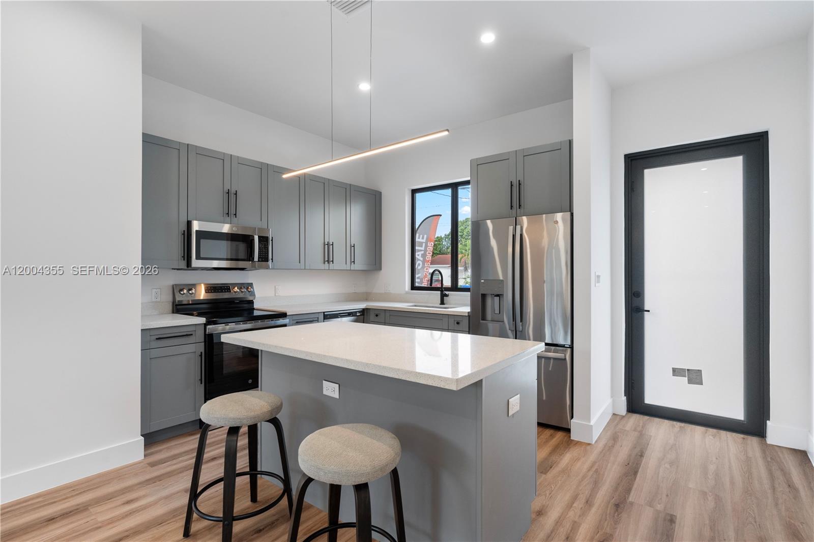 A modern kitchen features gray cabinets, stainless steel appliances, a quartz island, and wood flooring — 4518 NW 4 ST, Miami FL 33126, MIAMI, FL