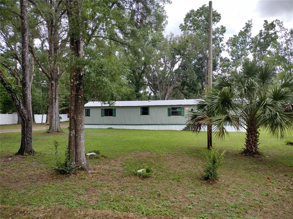 A single-story mobile home sits on a grassy lot surrounded by mature trees — 172 ESTATES AVENUE, BROOKSVILLE, FL