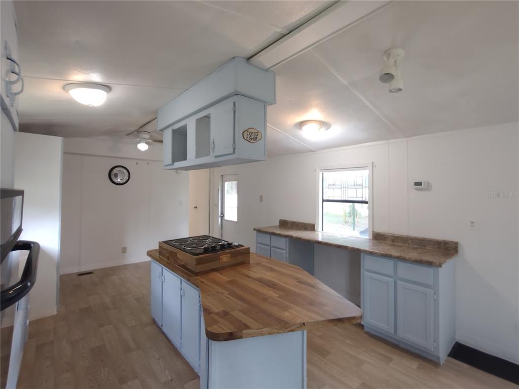 A kitchen features light blue cabinets, a wood-topped island with a cooktop, and laminate flooring — 172 ESTATES AVENUE, BROOKSVILLE, FL