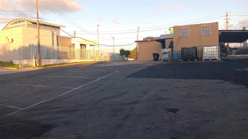 An asphalt parking lot sits in front of a tan commercial building with storage tanks — PR-167 KM 16.1 BUENA VISTA WARD - FALCON SECTOR, BAYAMON, PR