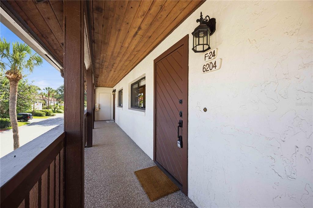 An exterior walkway with a wooden ceiling leads to a brown door labeled 6204 — 6204 COUNTRY CLUB DRIVE UNIT F24, LAKE WALES, FL