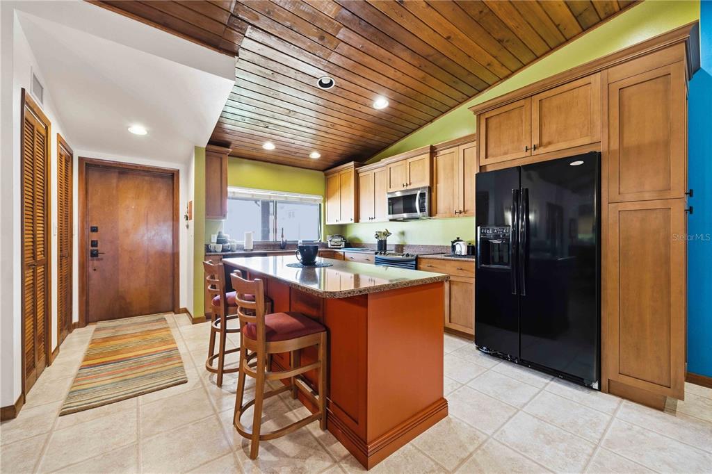 A kitchen features wood-paneled ceilings, light-colored cabinetry, a central island, and a black refrigerator — 6204 COUNTRY CLUB DRIVE UNIT F24, LAKE WALES, FL