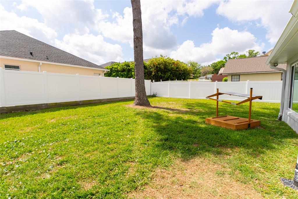 A grassy backyard features a large tree, a white vinyl fence, and a wooden sandbox — 1088 SW 32ND LANE, OCALA, FL